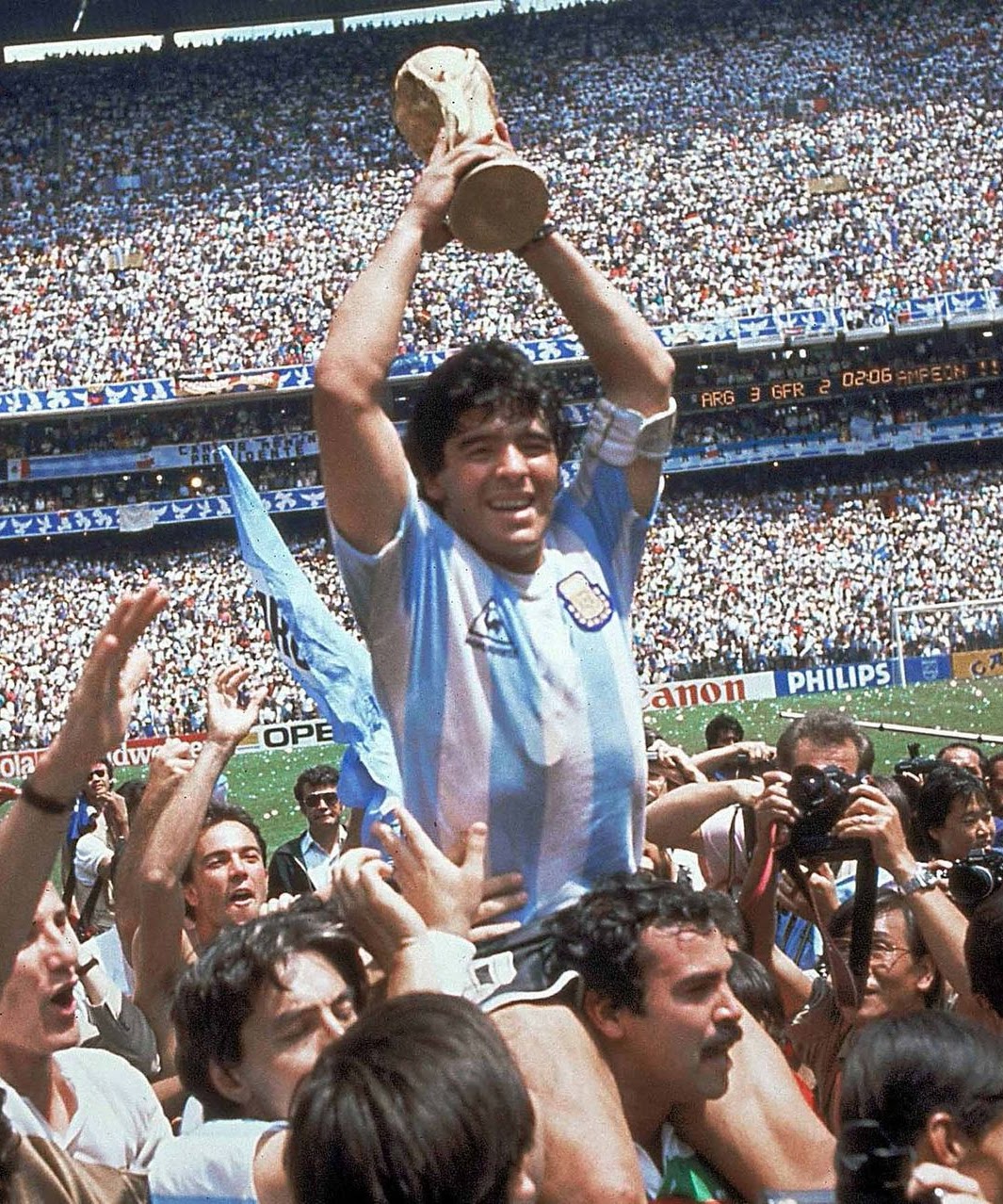 Maradona lifting the 1986 World Cup trophy surrounded by photographers